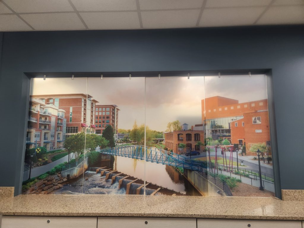 Set in a blue wall, 4 panels of glass are painted with a picture of Falls Park in Downtown Greenville