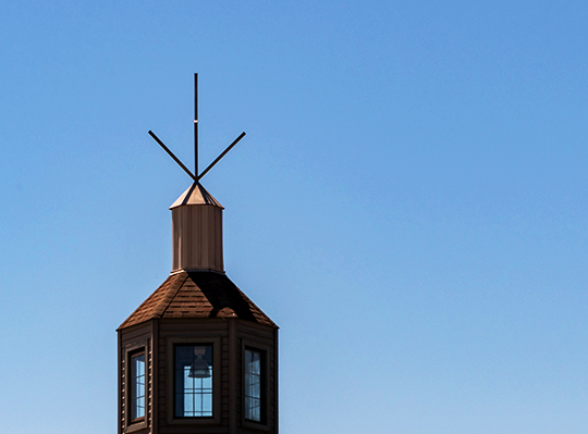 The top of a bell tower stands in front of a clear blue sky.