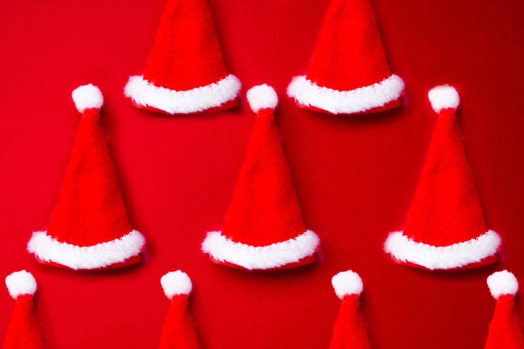 A red background with 3 rows of red Santa hats trimmed in white.