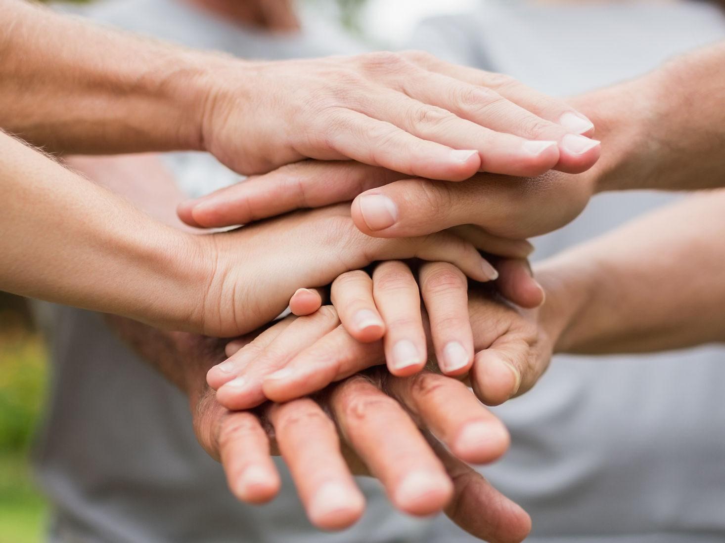 Three people stand in a circle with their hands stacked in the center. The torsos of the people are blurry in the background.