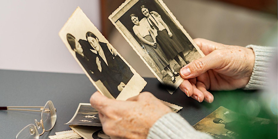 An elderly white womans hands hold two black and white photos featuring two women.