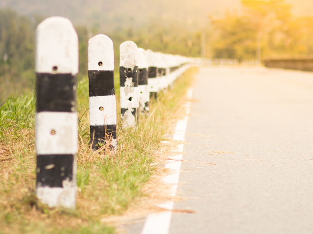 Black and white striped mileposts stand along the side of a road in hazy sunlight.