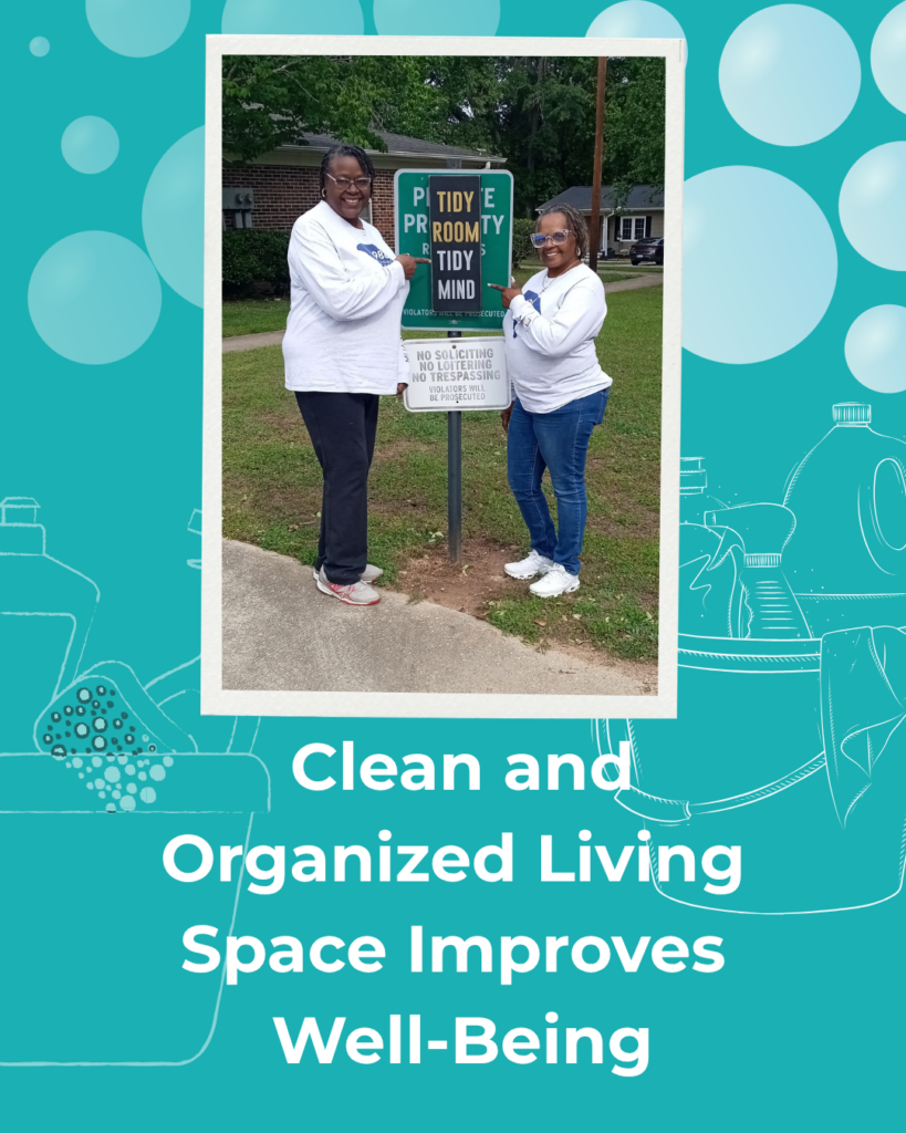 A photo of smiling black women wearing matching 988 shirts standing in front of a sign that says Tidy Room Tidy Mind and the words Clean and Organized Living Space improves Well-Being